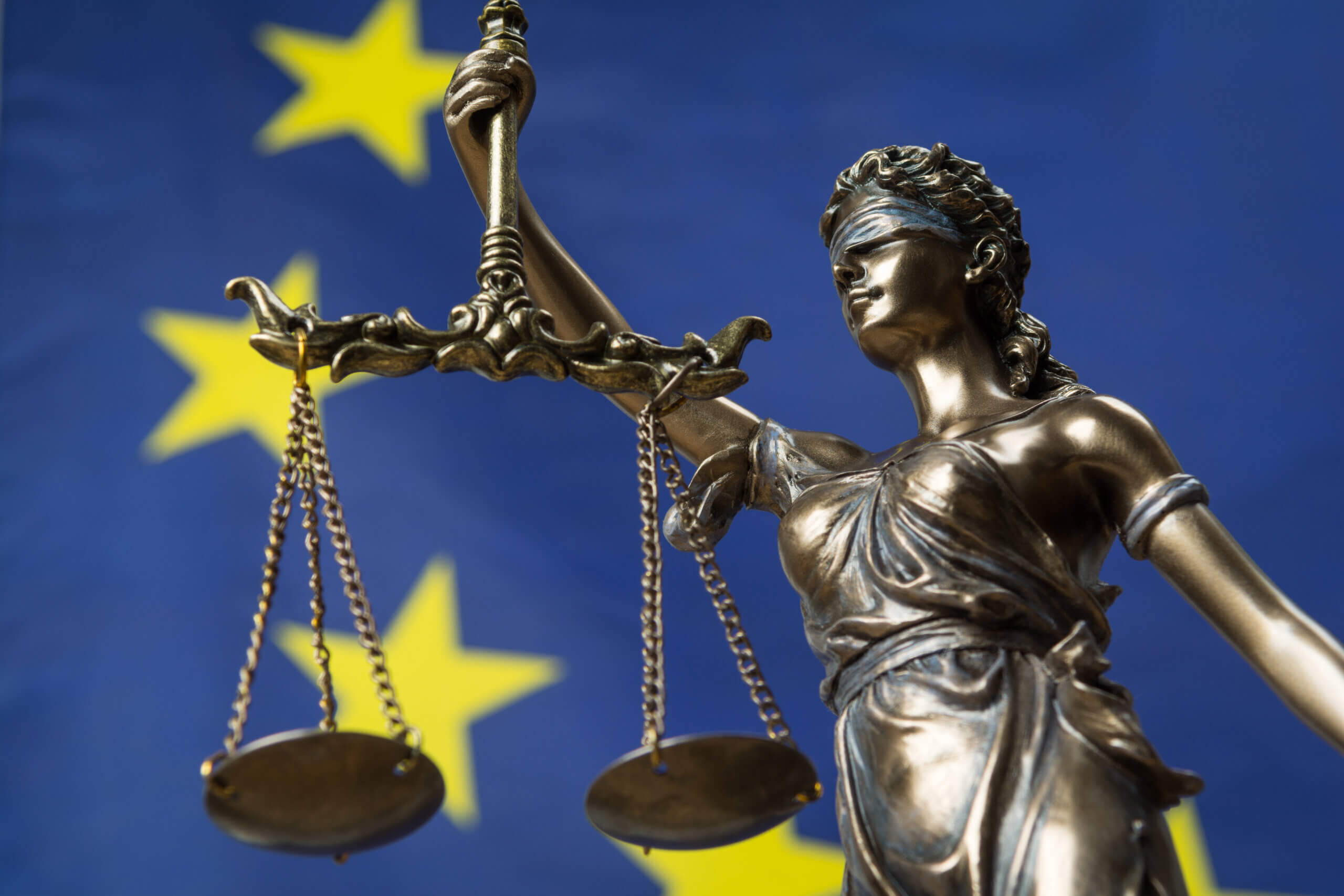 Statue of the blindfolded goddess of justice Themis or Justitia, against an European flag, as a legal concept